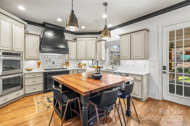 kitchen featuring appliances with stainless steel finishes, a breakfast bar, wooden counters, custom range hood, and a kitchen island