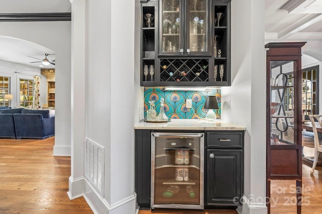 bar with light hardwood / wood-style flooring, ceiling fan, crown molding, beverage cooler, and backsplash