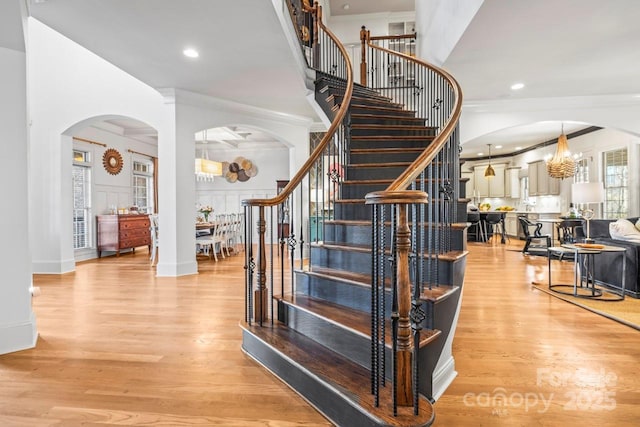 staircase with a high ceiling, ornamental molding, hardwood / wood-style floors, and a notable chandelier