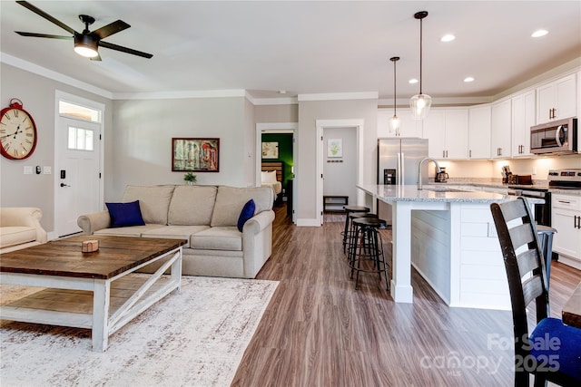 living area featuring baseboards, ornamental molding, wood finished floors, and recessed lighting