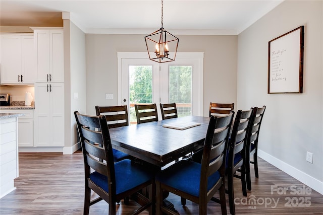 dining space featuring baseboards, ornamental molding, a notable chandelier, and wood finished floors