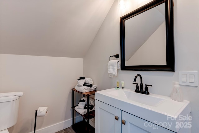 half bathroom with vaulted ceiling, vanity, toilet, and baseboards