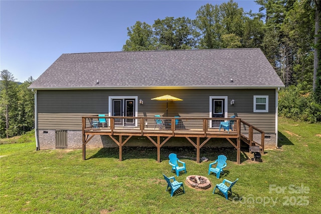 rear view of property featuring an outdoor fire pit, a lawn, a shingled roof, and a wooden deck