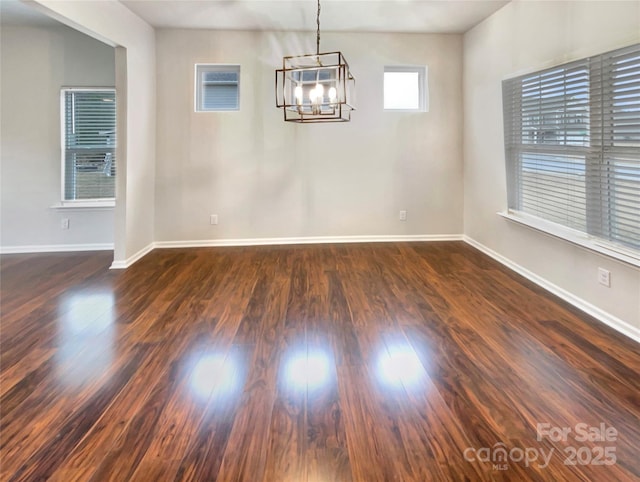 spare room with dark wood-type flooring, baseboards, and an inviting chandelier