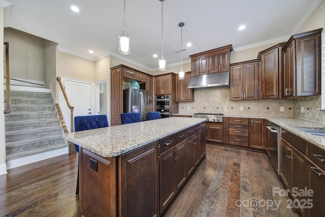 kitchen with a kitchen island, dark wood-type flooring, under cabinet range hood, light stone counters, and stainless steel appliances