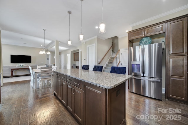 kitchen with ornamental molding, stainless steel refrigerator with ice dispenser, light stone counters, dark wood finished floors, and a center island