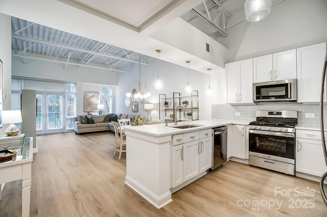 kitchen featuring appliances with stainless steel finishes, decorative light fixtures, sink, white cabinetry, and kitchen peninsula