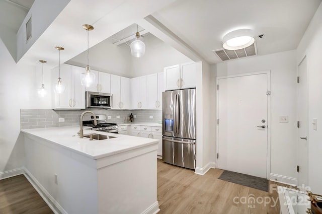 kitchen featuring appliances with stainless steel finishes, sink, pendant lighting, kitchen peninsula, and white cabinets