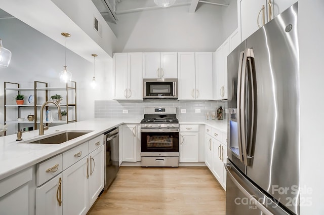 kitchen featuring appliances with stainless steel finishes, sink, white cabinetry, and hanging light fixtures