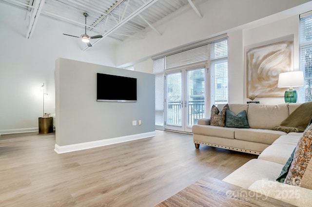 living room featuring hardwood / wood-style flooring, ceiling fan, a towering ceiling, and beam ceiling