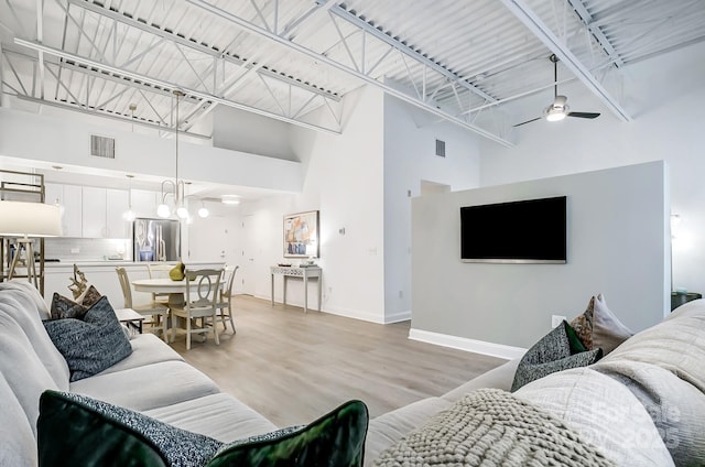 living room featuring light wood-type flooring, a towering ceiling, and ceiling fan