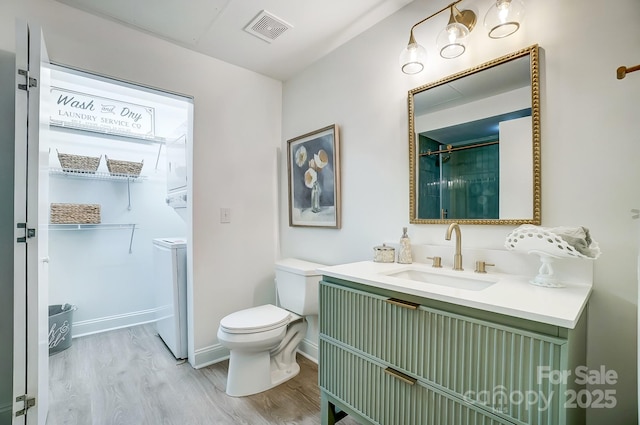 bathroom with toilet, vanity, wood-type flooring, and stacked washer and clothes dryer