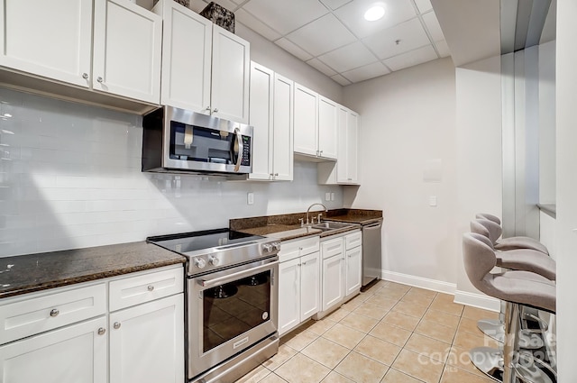 kitchen featuring sink, backsplash, dark stone counters, appliances with stainless steel finishes, and white cabinets