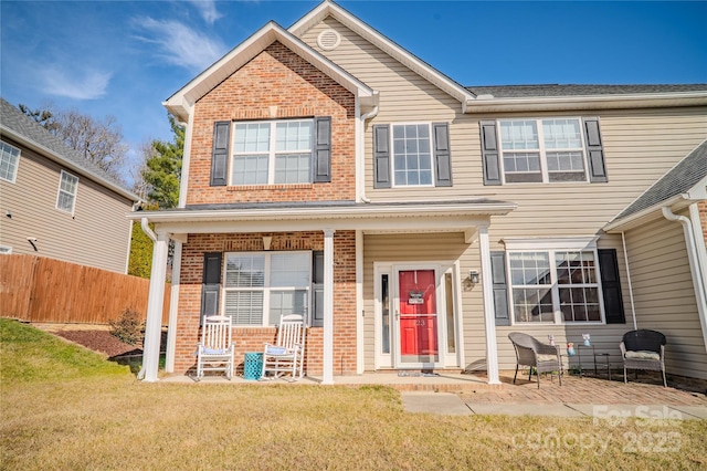 view of front of home with a porch, a front yard, brick siding, and fence