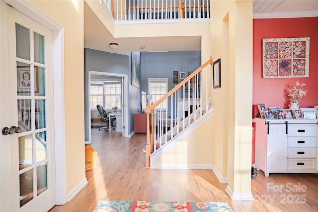 entrance foyer featuring wood finished floors, a towering ceiling, baseboards, ornamental molding, and stairway