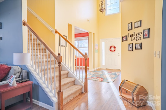 foyer featuring a towering ceiling, stairway, baseboards, and wood finished floors