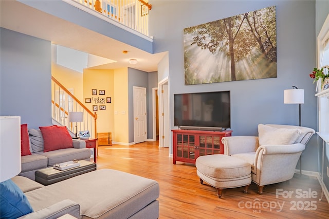 living area with a high ceiling, stairway, wood finished floors, and baseboards