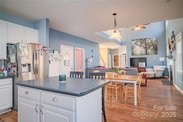 kitchen with wood finished floors, a kitchen island, white cabinetry, open floor plan, and dark countertops