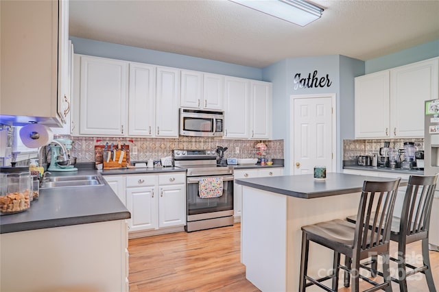 kitchen with stainless steel appliances, dark countertops, white cabinetry, and a kitchen bar