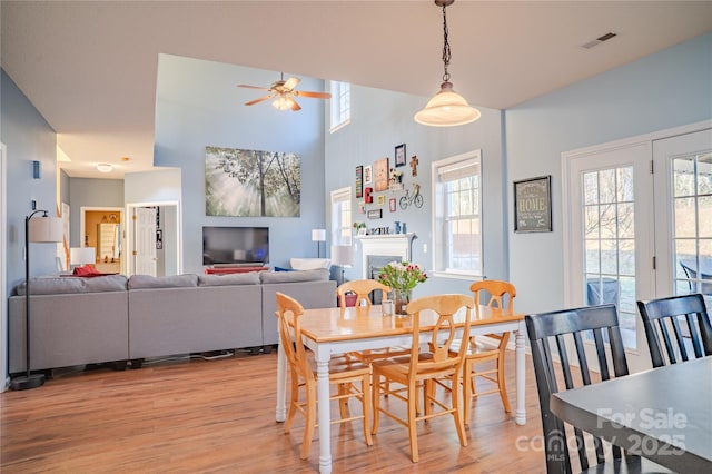 dining space with light wood finished floors, visible vents, a towering ceiling, ceiling fan, and a fireplace