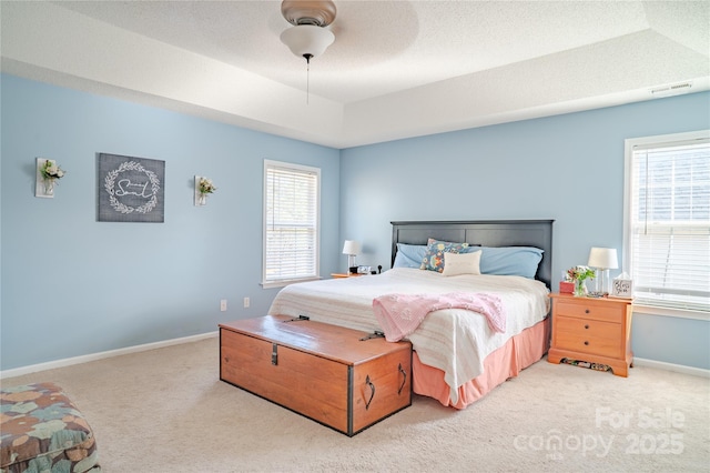 bedroom featuring a raised ceiling, multiple windows, and carpet flooring