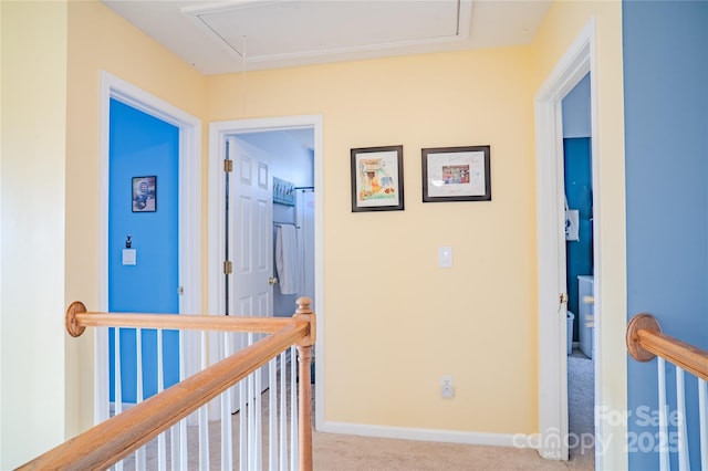 hallway with carpet flooring, an upstairs landing, attic access, and baseboards