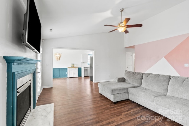 living room featuring a premium fireplace, vaulted ceiling, dark wood-type flooring, and ceiling fan