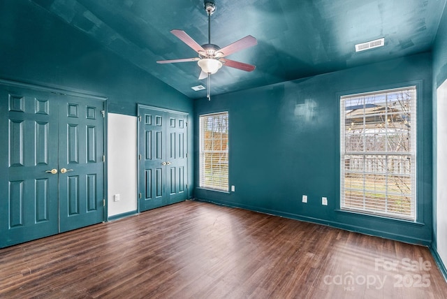 unfurnished bedroom with two closets, vaulted ceiling, ceiling fan, and hardwood / wood-style flooring