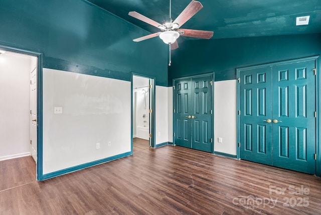 unfurnished bedroom featuring ceiling fan, hardwood / wood-style floors, high vaulted ceiling, ensuite bathroom, and multiple closets