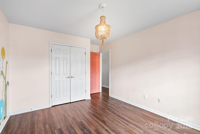 unfurnished bedroom featuring dark wood-type flooring, a closet, and a chandelier