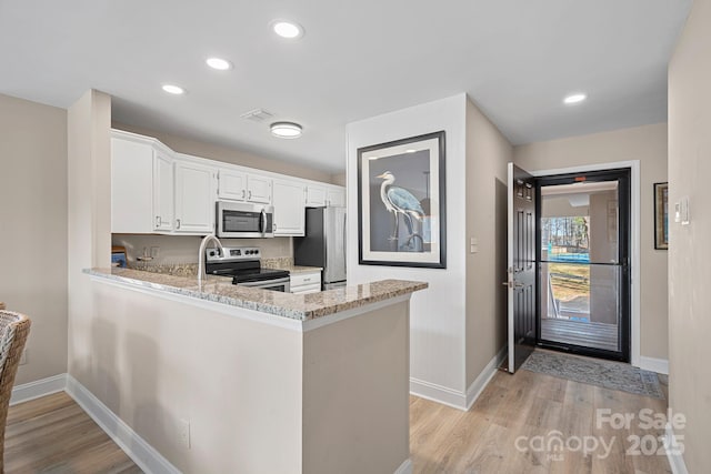 kitchen with white cabinetry, kitchen peninsula, stainless steel appliances, light stone countertops, and light hardwood / wood-style floors