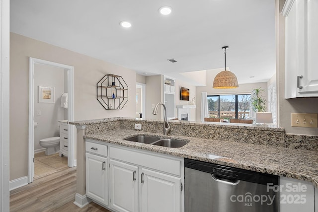 kitchen featuring decorative light fixtures, dishwasher, sink, white cabinets, and light stone counters