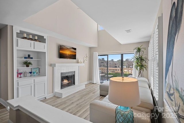 living room featuring high vaulted ceiling, built in features, a tile fireplace, and light wood-type flooring