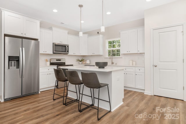 kitchen featuring light countertops, appliances with stainless steel finishes, white cabinetry, and decorative light fixtures