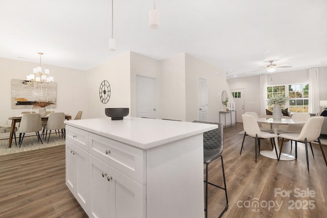 kitchen with dark wood-type flooring, white cabinets, light countertops, a center island, and decorative light fixtures