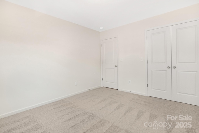 unfurnished bedroom featuring a closet, light colored carpet, and baseboards