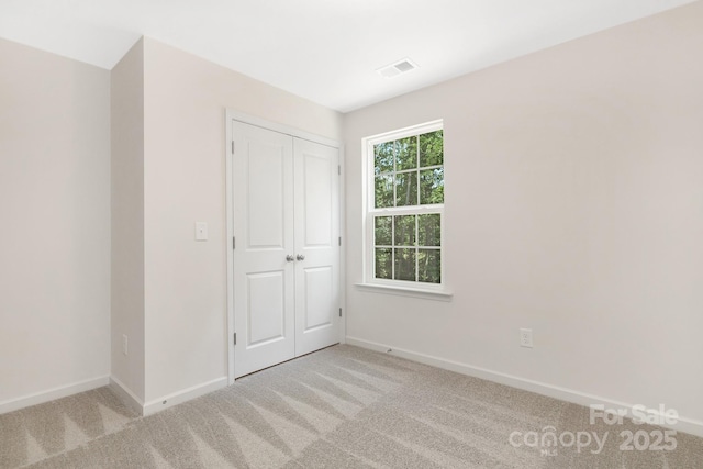 unfurnished bedroom with light carpet, a closet, visible vents, and baseboards