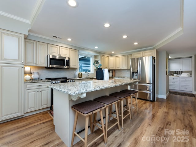 kitchen with light wood-style flooring, stainless steel appliances, a kitchen breakfast bar, ornamental molding, and a center island