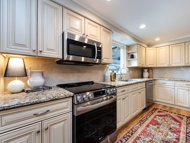 kitchen with backsplash, appliances with stainless steel finishes, a sink, light stone countertops, and light wood-type flooring