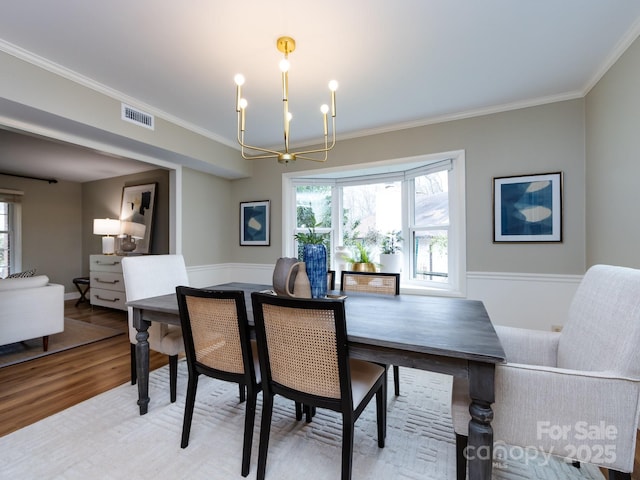 dining area with visible vents, ornamental molding, a notable chandelier, and wood finished floors