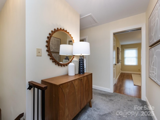 hall featuring attic access, carpet flooring, and baseboards