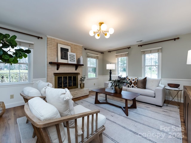 living area with light wood finished floors, baseboards, visible vents, a brick fireplace, and a notable chandelier