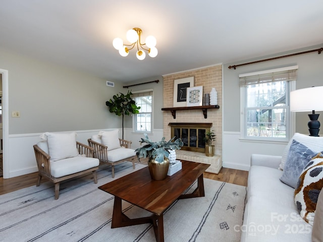 living room featuring a chandelier, a brick fireplace, wood finished floors, and baseboards