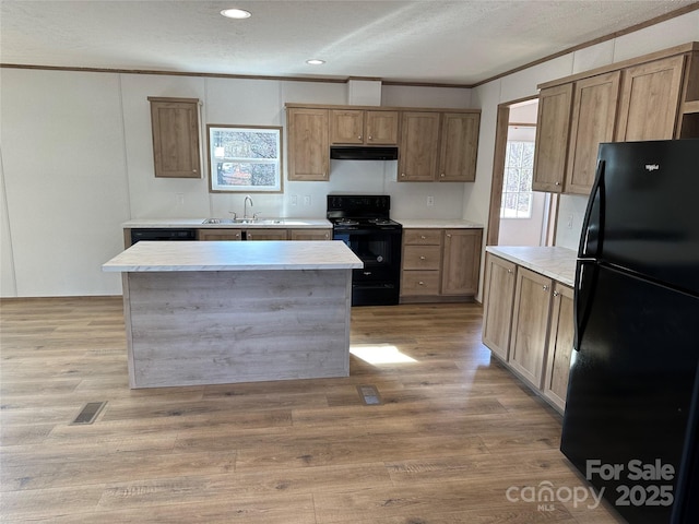 kitchen featuring range hood, light wood finished floors, visible vents, a sink, and black appliances