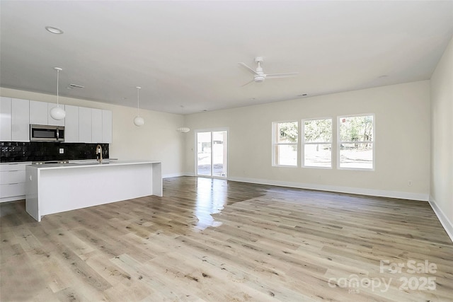 kitchen featuring tasteful backsplash, a center island with sink, white cabinets, and light wood-type flooring