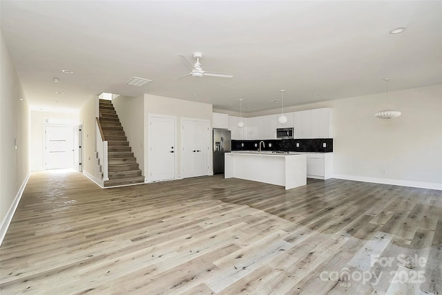 kitchen featuring hanging light fixtures, stainless steel appliances, white cabinets, a center island with sink, and decorative backsplash