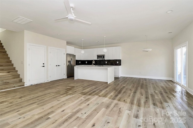 kitchen featuring pendant lighting, white cabinetry, appliances with stainless steel finishes, and a kitchen island with sink