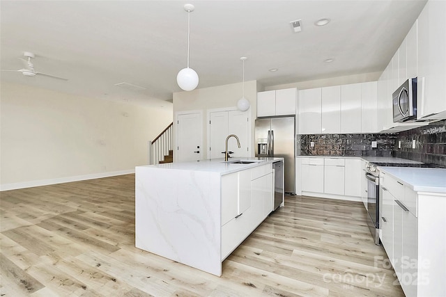 kitchen featuring pendant lighting, sink, appliances with stainless steel finishes, a kitchen island with sink, and white cabinets