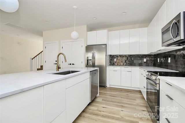 kitchen featuring appliances with stainless steel finishes, white cabinetry, sink, hanging light fixtures, and light hardwood / wood-style floors