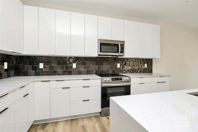 kitchen featuring stainless steel appliances, white cabinetry, backsplash, and light hardwood / wood-style flooring